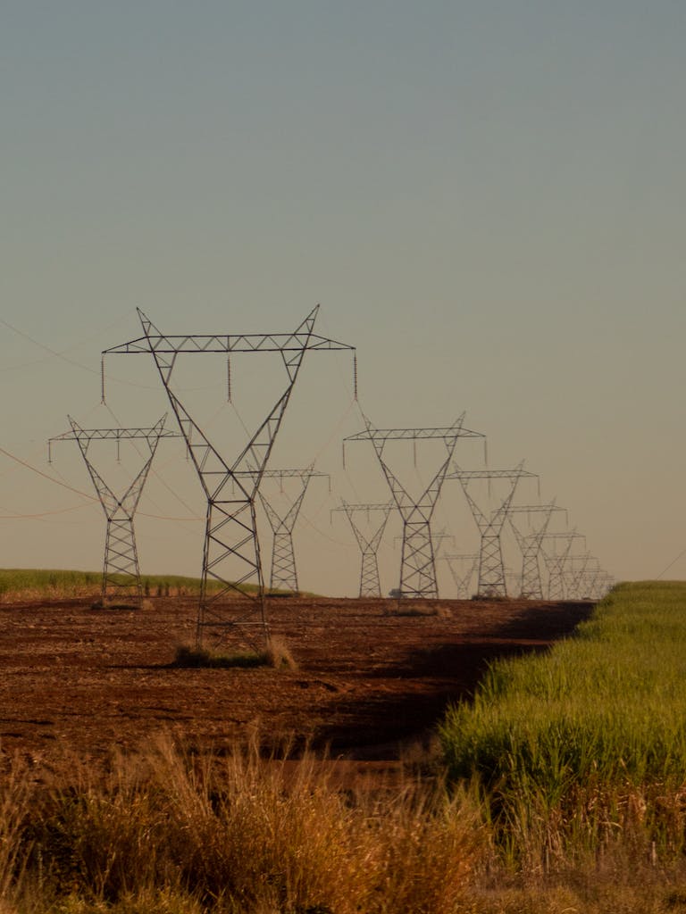 Power lines with wires located on ground near grassy field against cloudless sky in countryside in summer day in nature