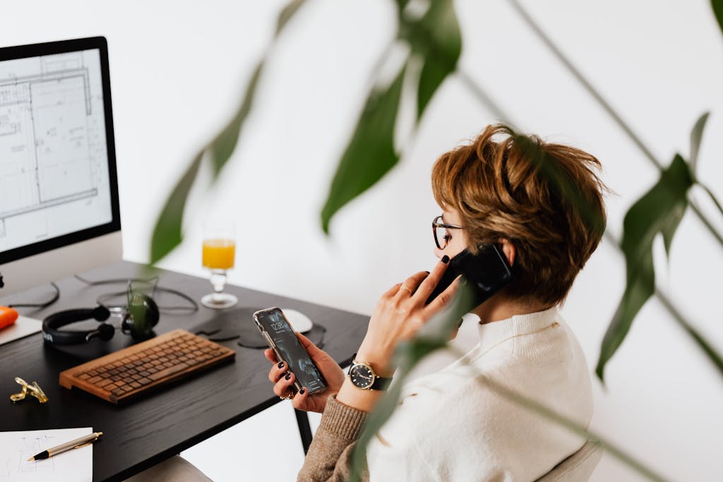 Busy female talking on smartphone and checking messages during work in contemporary office