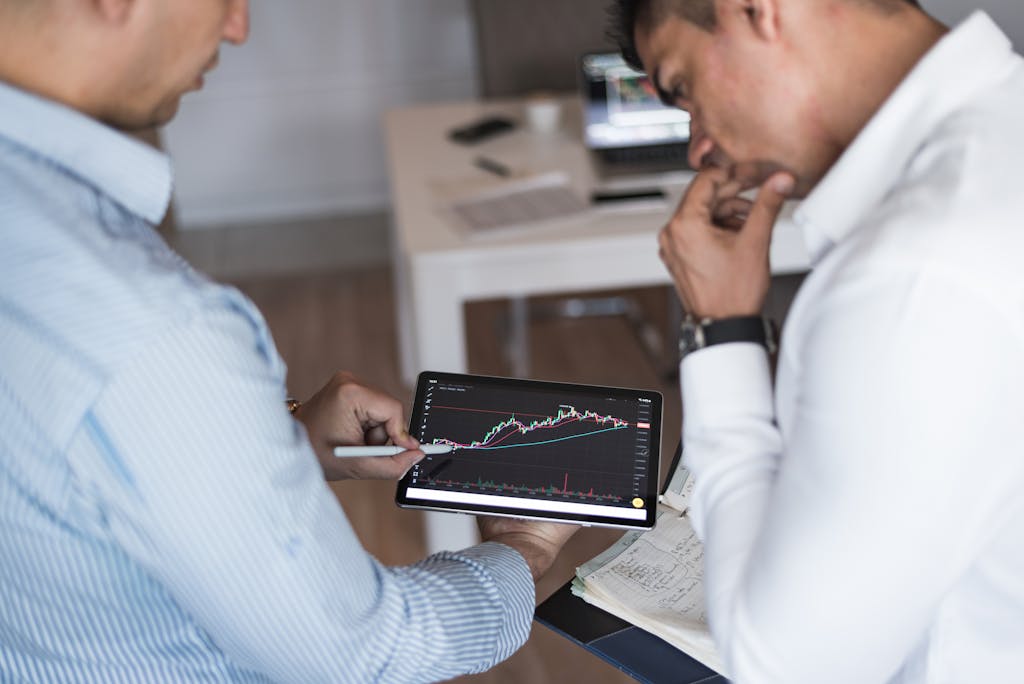 Two businessmen using a tablet for online trading analysis in an office setting.