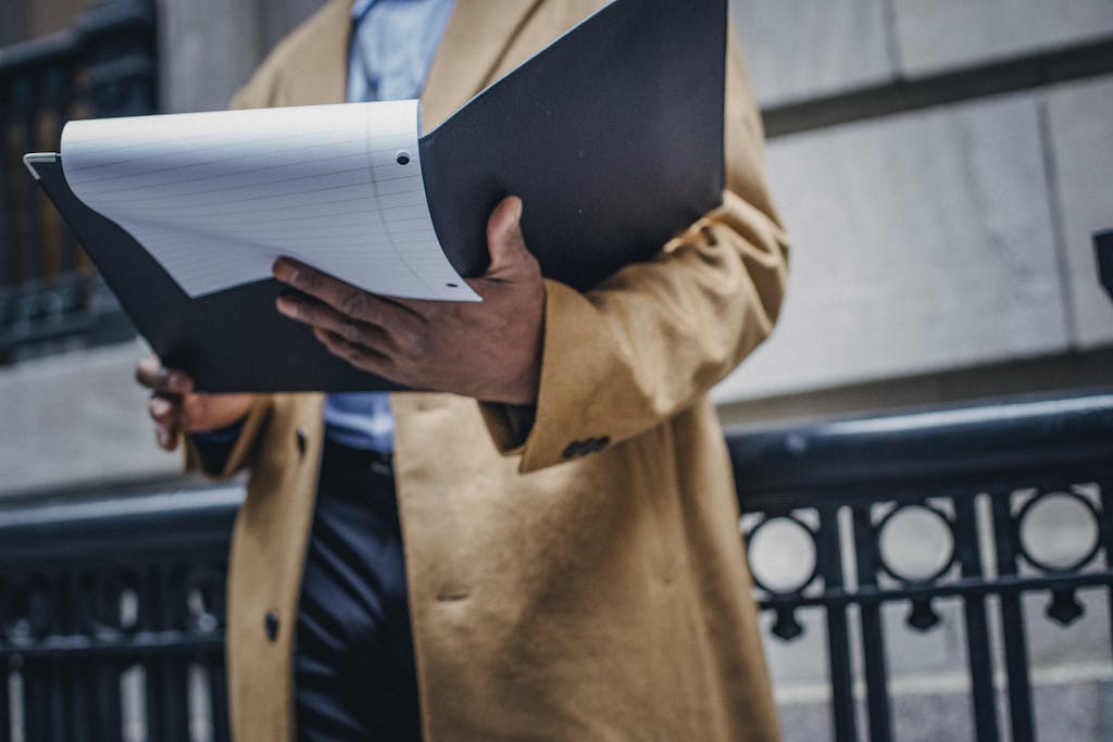 A businessman holding a folder with papers outside a city building.